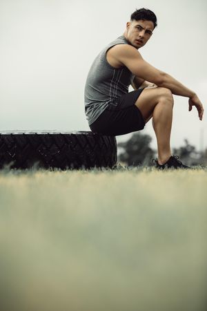 Young man sitting on big tire outdoors after a workout