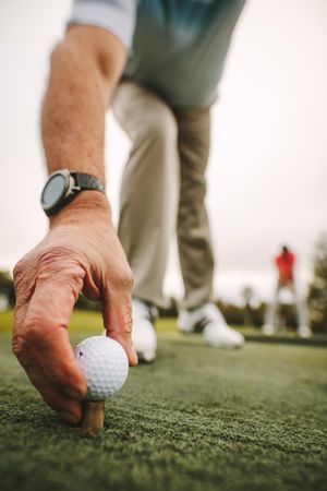 Mature male golf player placing golf ball on tee