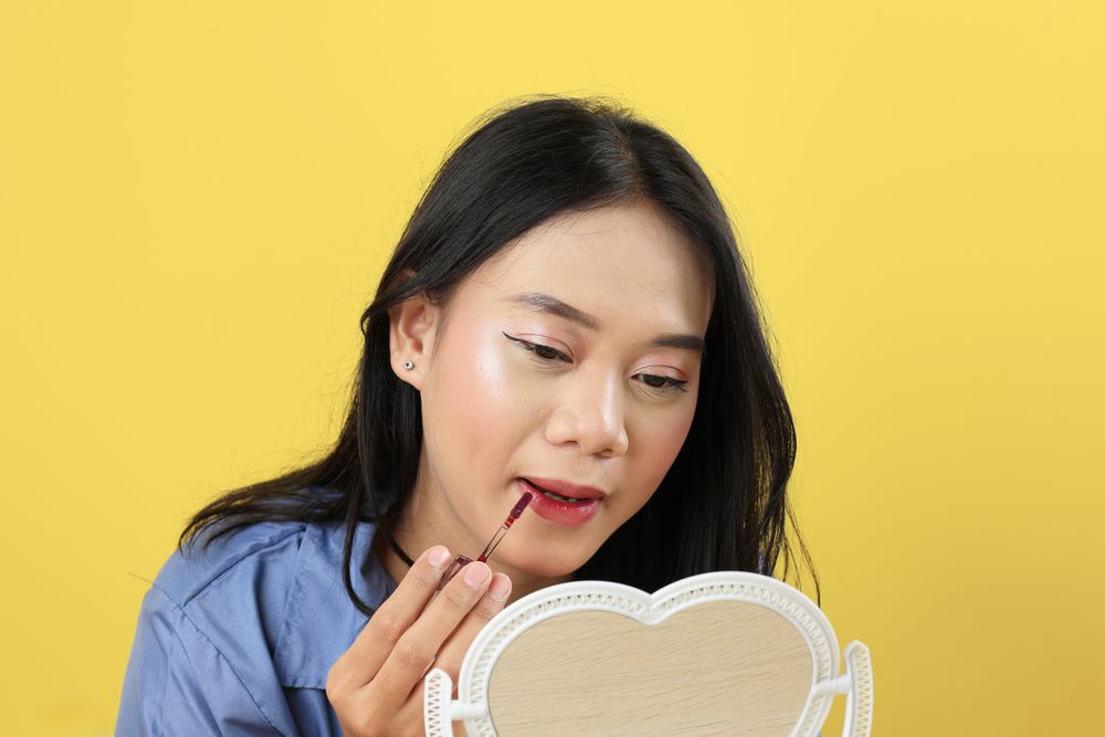 Asian Young Woman, Make Up Face by Applying Red Lipstick, Lips Balm on her Lips using Lip Applicator.