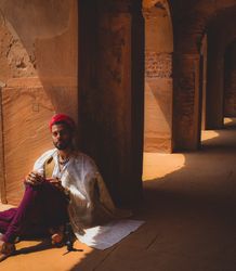 Man in traditional outfit sitting beside pillar