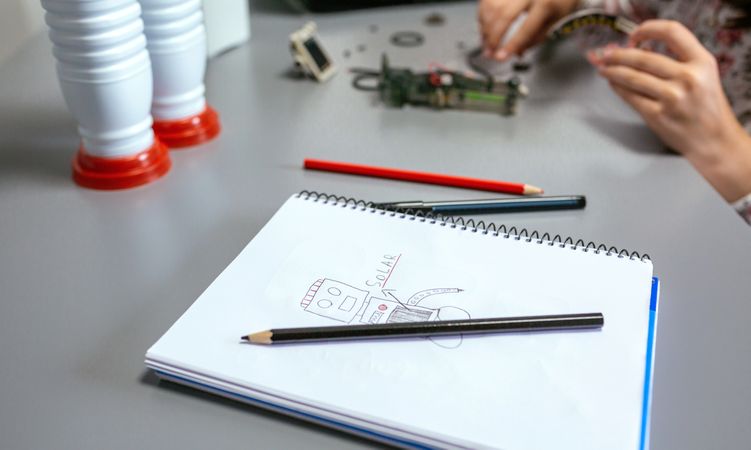 Robot draw by child on notebook and student assembling pieces of toy in a robotics class