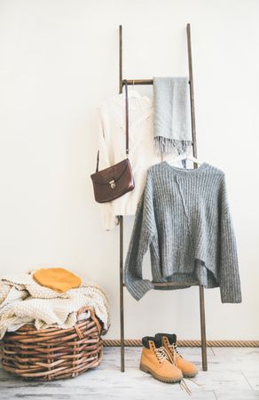 Woolen sweaters, grey scarf and winter boots on modern garment rack, with thatched laundry basket