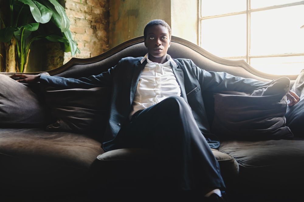 Portrait of a Black woman with short hair sitting on the couch legs crossed and looking at the camera
