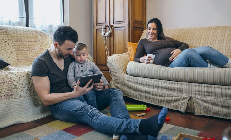 Father looking at tablet with little son while the pregnant mother drinks tea
