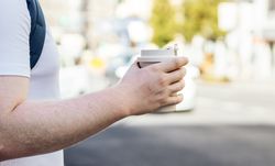 Close-up of the hand of an unrecognizable man holding a takeaway coffee in the city