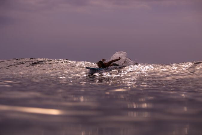 Man on surf board on waving water at sunset