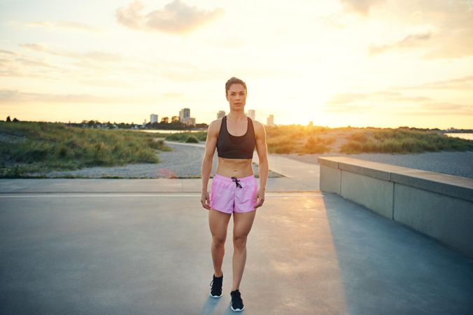 Muscular woman standing with the sunrise and city in the background