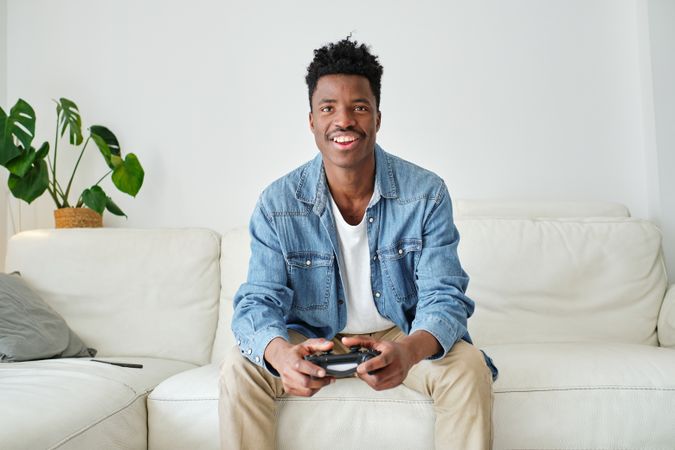 Happy Black man with game pad playing on sofa