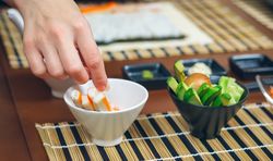 Chef reaching for crab meat from bowl as she prepares sushi rolls