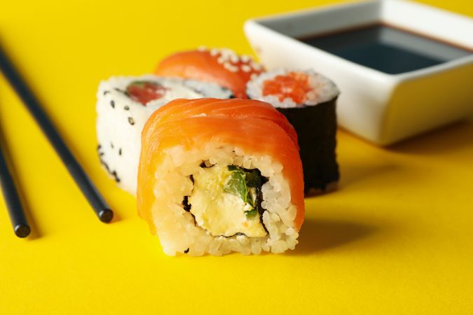 Sushi rolls, chopsticks and soy on yellow background, close up