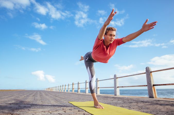 Woman doing virabhadrasana yoga pose at the seaside