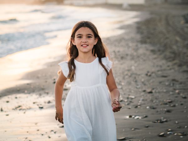 Excited girl running along beach in daylight