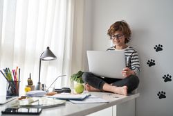 Happy barefoot boy looking at screen and using laptop at home