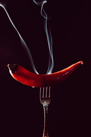 red chili pepper on fire in fork on a dark background