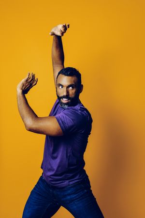 Black man in yellow studio with arms up to his side in martial art position, vertical composition