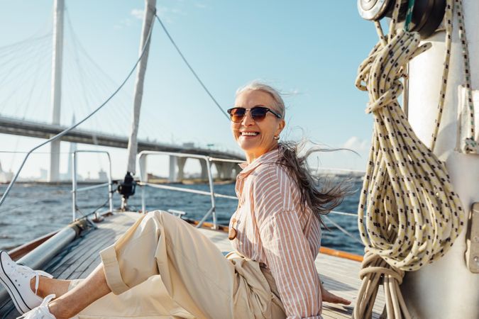 Stylish mature woman sitting on a yacht bow with bridge in background