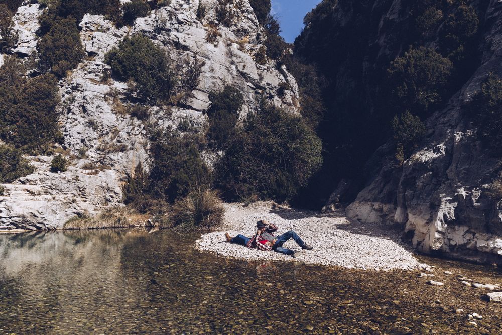 Positive woman and man resting on stone shore near river