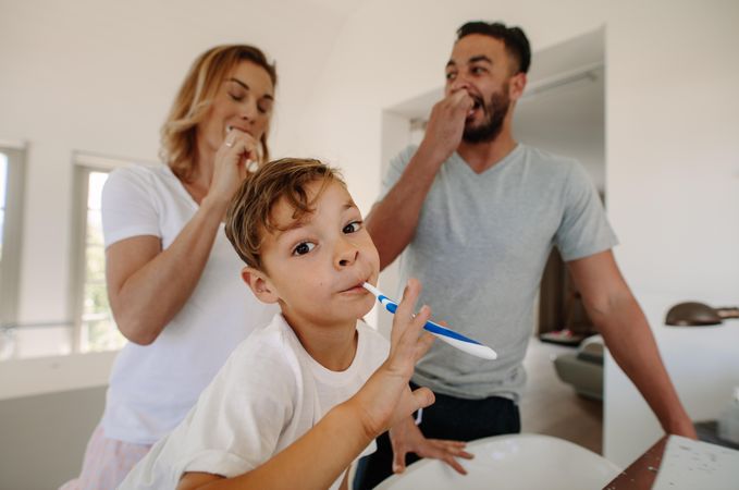 Little boy brushing teeth with his parents in bathroom