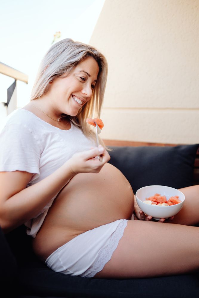 Faceless pregnant woman eating fruits with fork