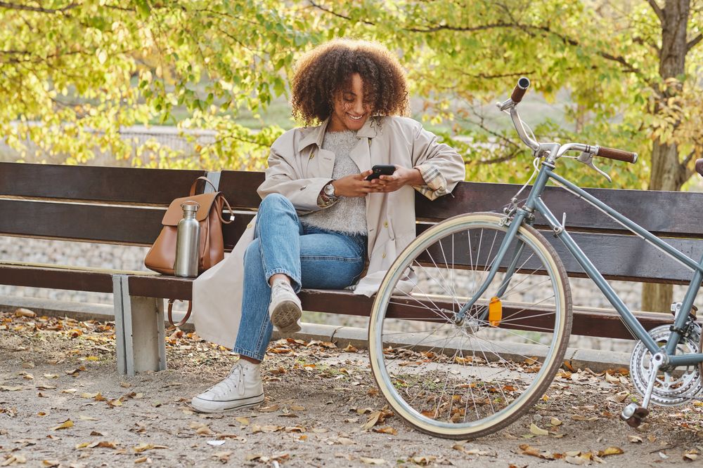 Smiling Black Latina woman sitting on bench with smartphone