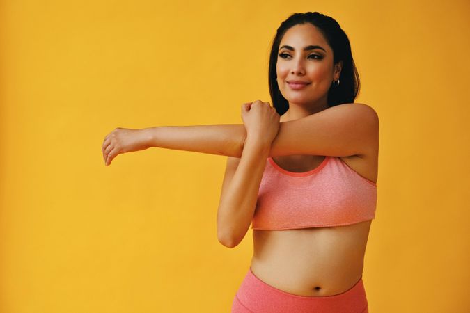 Hispanic woman in yoga clothes stretching her arm in yellow studio