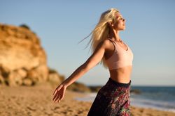 Blonde woman stretching her arms facing the ocean on beach at sunset