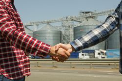Businessmen shake hands against silos. Agriculture business