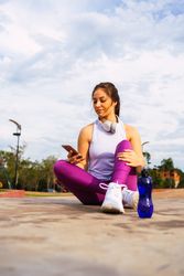 Young woman sitting on sports ground while browsing smartphone