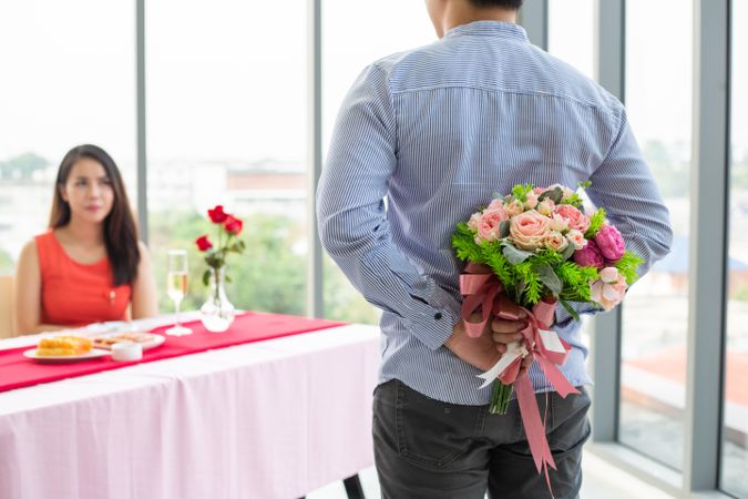 Man hiding bouquet from woman behind his back during romantic meal