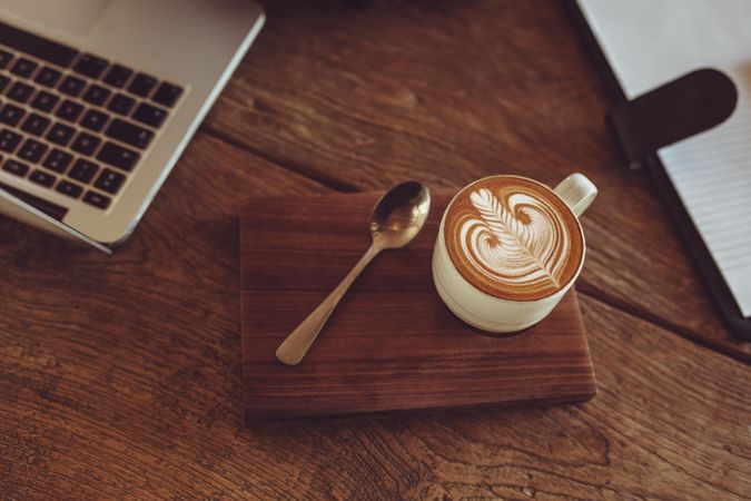 Cup of latte coffee with milk foam art pattern on wood tray