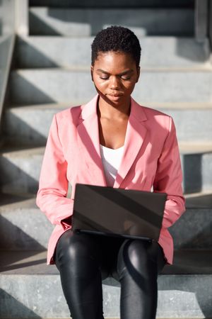 Female in pink suit working on shadowy stairs outside, vertical composition