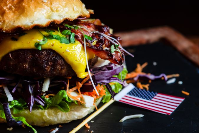 Close up of bacon burger with melted cheese and vegetables with mini flag