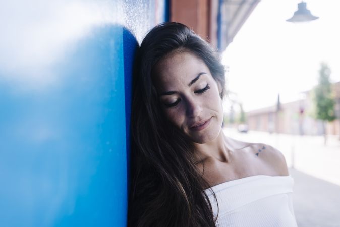 A young smiling woman leaning against a blue wall looking down