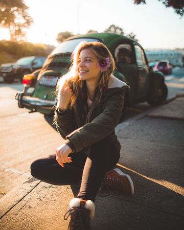 Smiling woman sitting on sidewalk near green beetle car