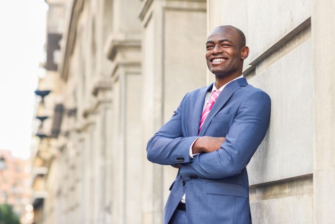 Happy male in business attire leaning on wall with arms closed, copy space