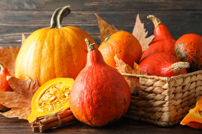Pumpkins in straw basket on wooden background, close up