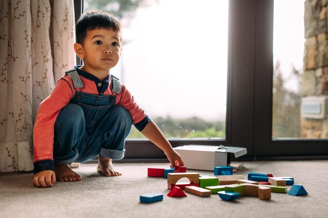Sweet little boy sitting on floor with colorful wooden blocks lying in front