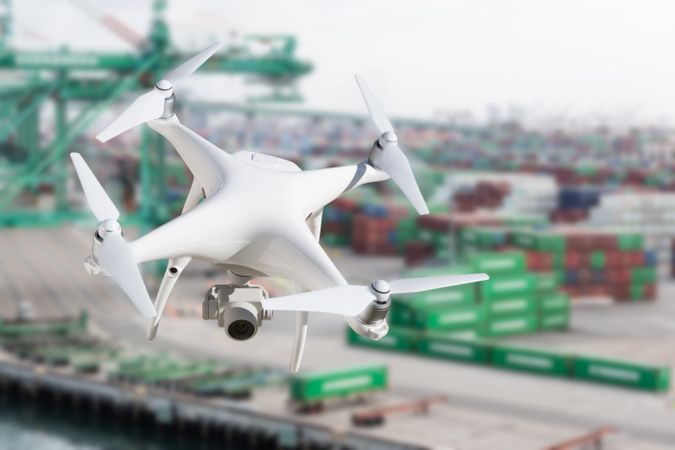 Unmanned Aircraft System Quadcopter Drone In The Air Near Large Shipping Vessel and Dock with Crates