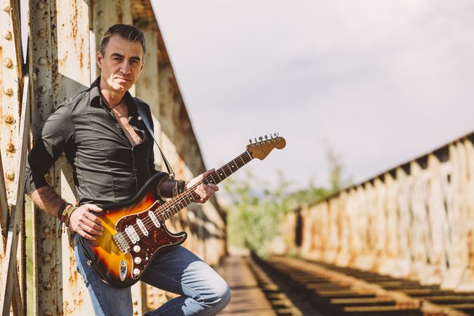 Man with guitar standing on bridge