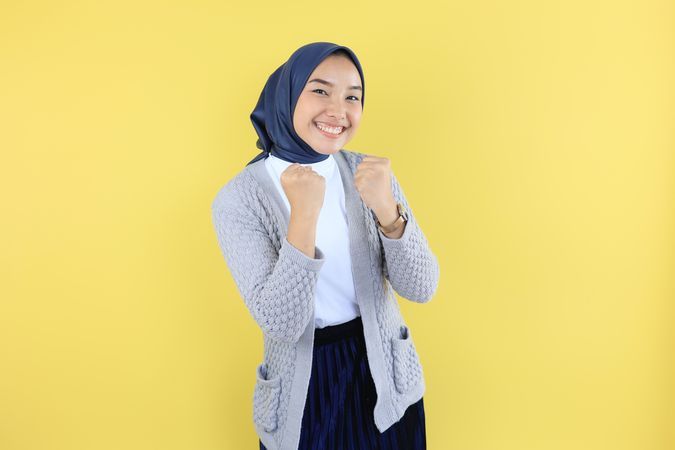 Excited Young Asian Female Wearing Scarf with Raised Hands Celebrating Success.