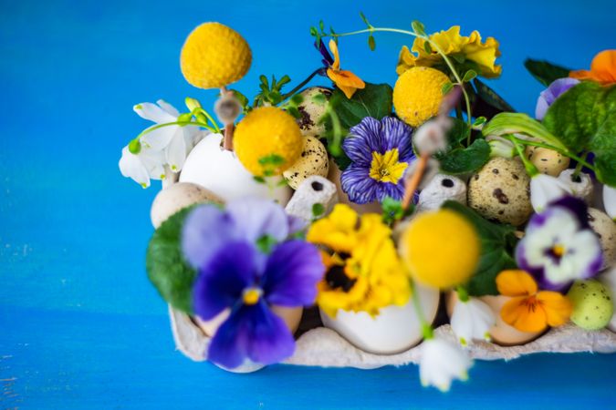 Close up Easter holiday card concept with egg carton covered with bright flowers on blue table