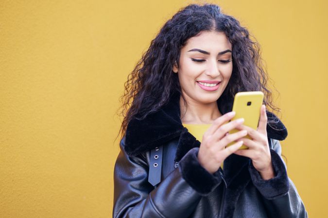 Happy female standing with yellow phone in front of yellow background