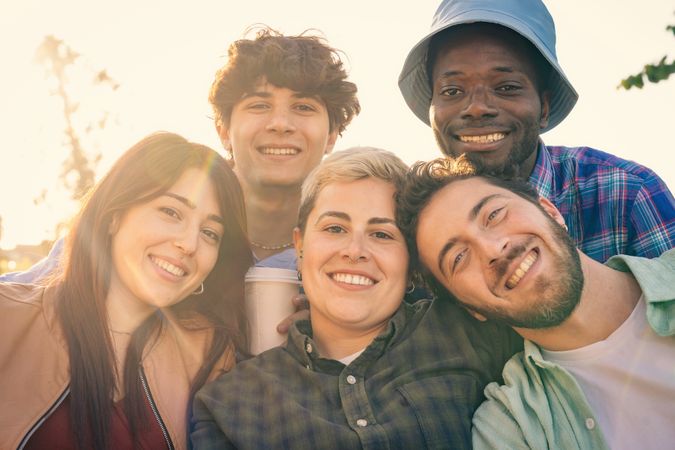 A happy diverse group of friends smiling together in the warm sunlight at sunset.