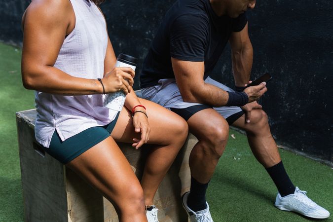 Anonymous ehnic woman drinking water near athlete using smartphone