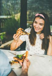 Couple eating pizza al fresco with wine with woman smiling holding pizza