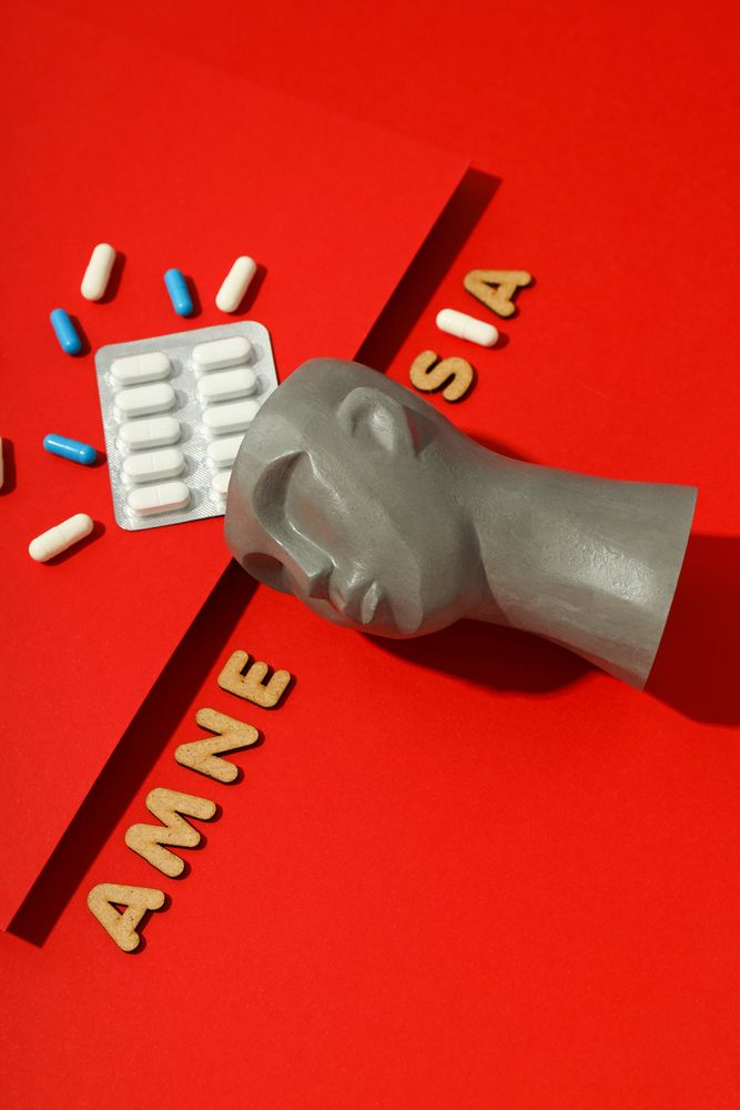 Model of bust with pills on red background and the words “Amnesia,” vertical composition