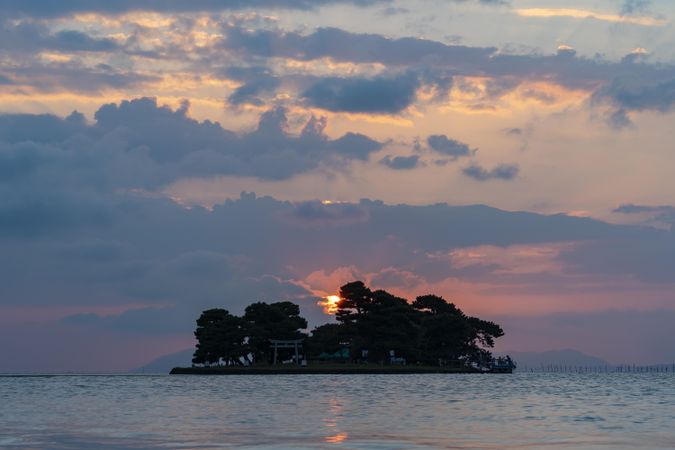 Sun setting behind a small island in the ocean on a cloudy day