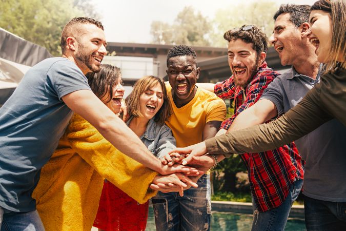 Joyful multi-ethnic teamwork of people having fun joining hands together