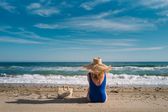 Woman in blue swimsuit and hat on sandy beach