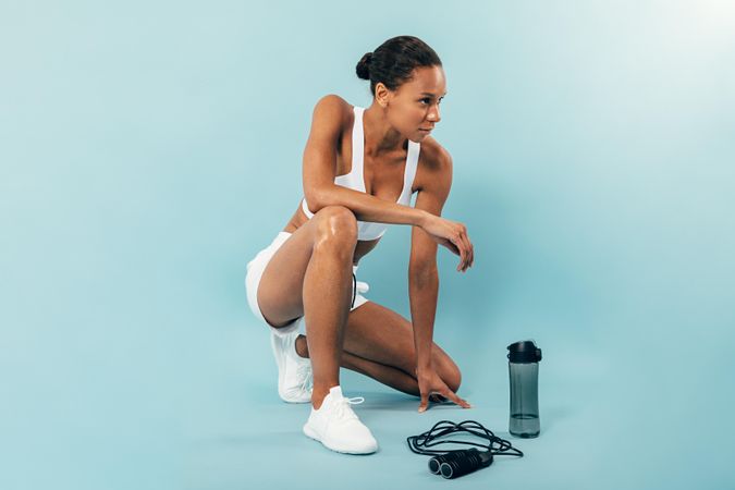 Fit woman sitting in blue studio after working out with jump rope and water bottle
